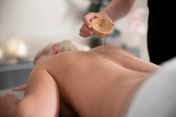 Aplicação de óleo vegetal morno nas costas durante passo a passo da massagem ayurveda Abhyanga.